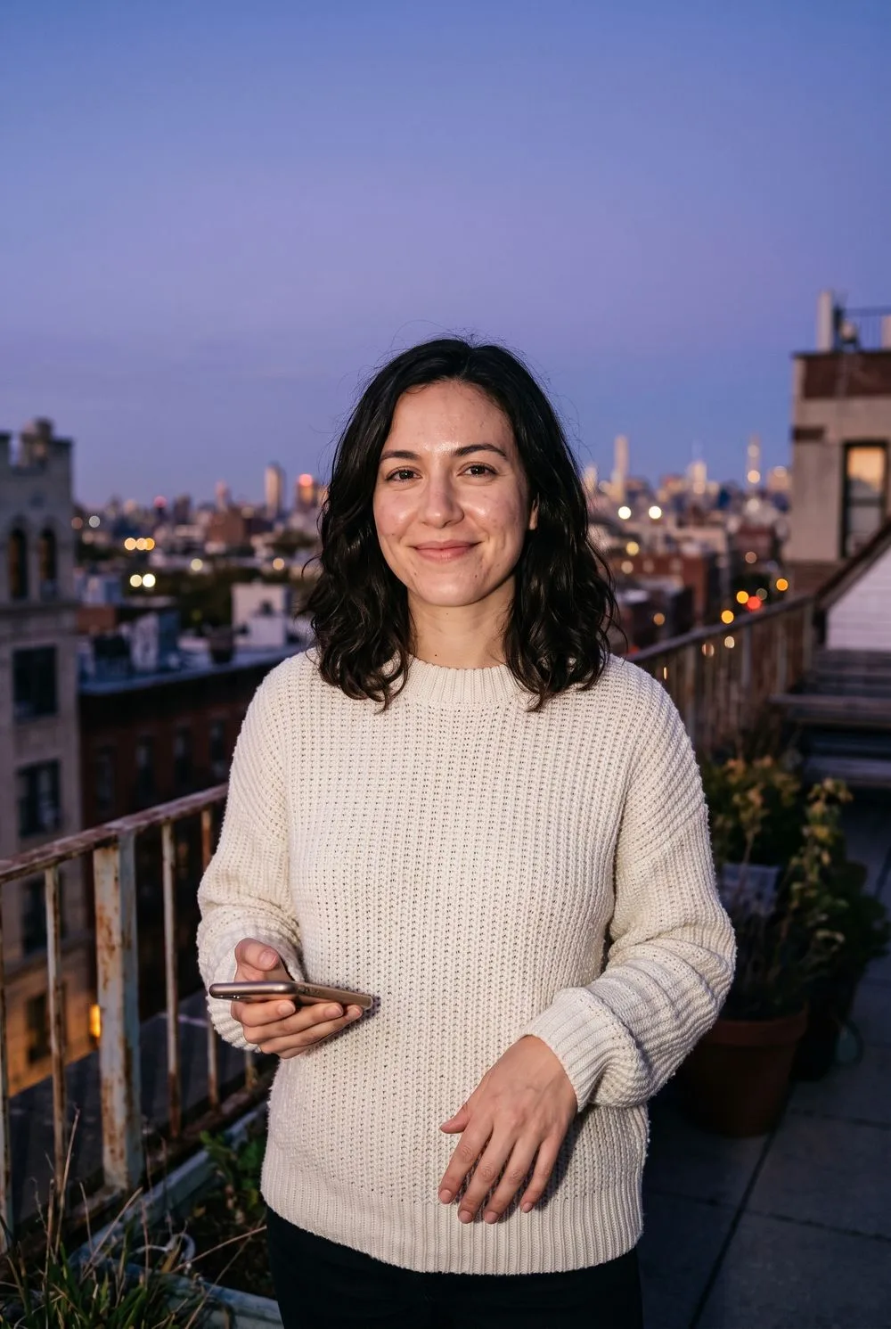 Woman in a cream sweater on a city rooftop at blue hour, lit by a soft on-camera flash